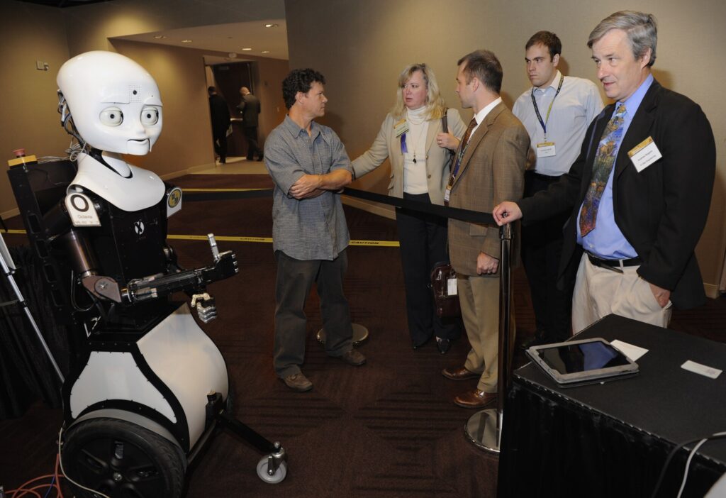 ARLINGTON, Va. (Nov. 9, 2010) Greg Trafton, center, a cognitive scientist with the Naval Research Laboratory, discusses Octavia, left, an MDS or mobile, dexterous, social robot, to exhibit hall attendees during day two of the Office of Naval Research 2010 Naval Science and Technology Partnership Conference. Octavia is part of the Office of Naval Research human robotics interaction research program which focuses on the abilities of teams of humans and autonomous systems to communicate clearly, collaborate to solve problems, and interact via means both locally and remotely. (U.S. Navy photo by John F. Williams/Released)