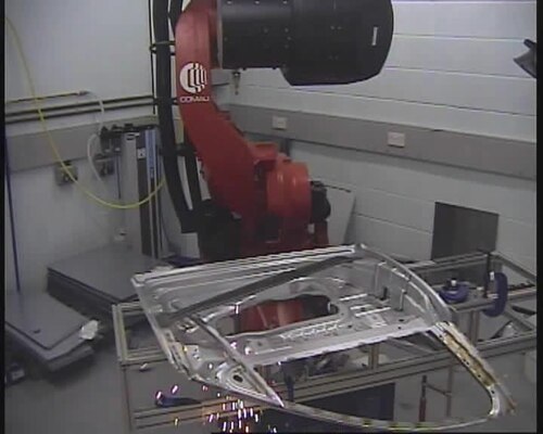 A steel car door is welded using remote laser welding, as part of an experiment in the Technology Strategy Board funded 'Remote Fibre Laser Welding Project', run by Warwick Manufacturing Group at the University of Warwick. An externally generated laser beam is fed into the robot by the yellow cable behind and to the left of the robot. Lenses and mirrors in the robot's arm focus the beam at a target point, and the intense energy causes welding to occur.