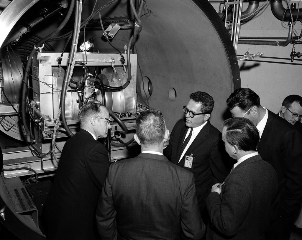 In February 1964, the Plasma Flow Research Laboratory at NASA's Jet Propulsion Laboratory in Pasadena, Calif., was completed. It was located in Building 112 by the East Gate in what was once rocket motor test cell B. It included a 7-foot-by-14-foot stainless steel cylindrical vacuum chamber with port holes on the sides to view and photograph the tests. In this photo, Gary Russell, a group supervisor in the Propulsion Research Section, discusses the plasma facility with JPL Director William Pickering, Deputy Director Brian Sparks, Assistant Director for Research and Advanced Development Frank Goddard, and Propulsion Research Section Chief Don Bartz. Lab-Oratory, the JPL employee newspaper, covered the opening of this new facility, describing how plasma can be generated by bodies entering an atmosphere at high speed and in the plasma lab by electrical discharge. The plasma facility at JPL could create thermally ionized gases at temperatures up to 30,000 degrees Fahrenheit. Findings from the plasma program were to be applied to power and propulsion devices, and Earth re-entry problems (thermal protection, communication blackout and electrical breakdown). This was a $1.6 million JPL task – part of the larger NASA plasma research and development program. Plasma demonstration attended by Dr. William Pickering, Mr. Sparks, and Goddard. March 4, 1964 Requested by: Collela Photo by: J. Rayle